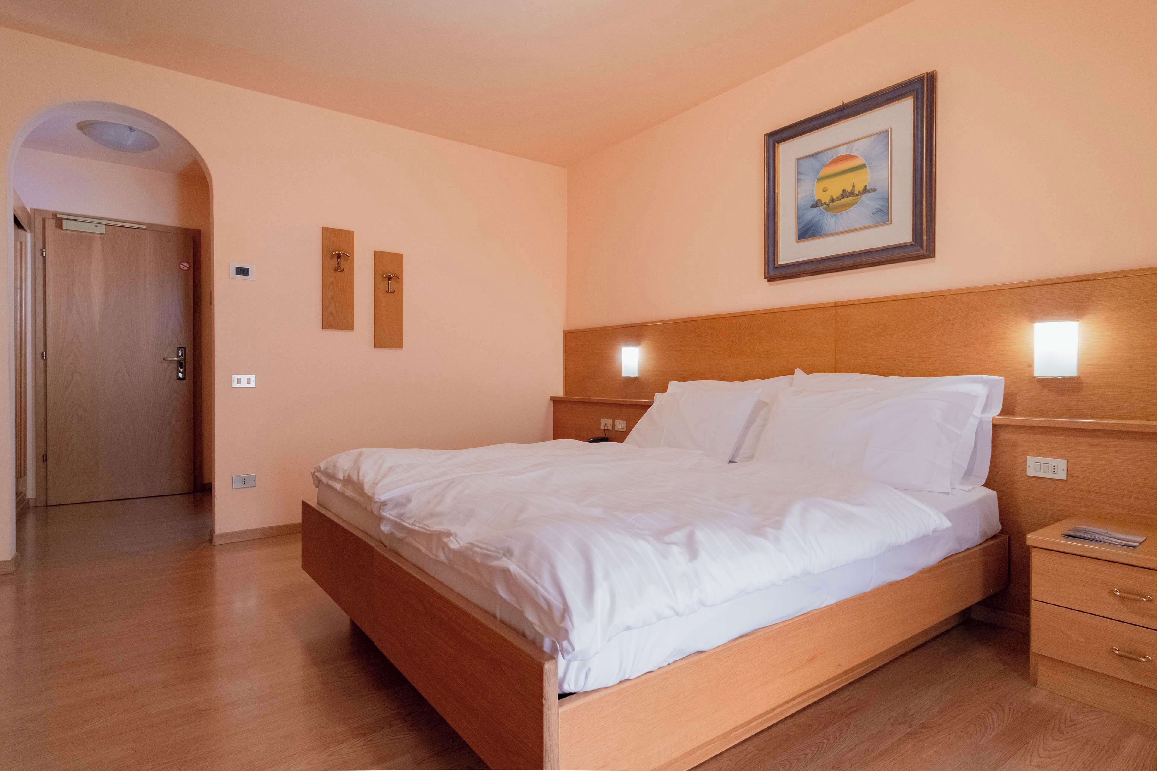A hotel room with a wooden bed, bedside tables, and a framed picture on the wall.