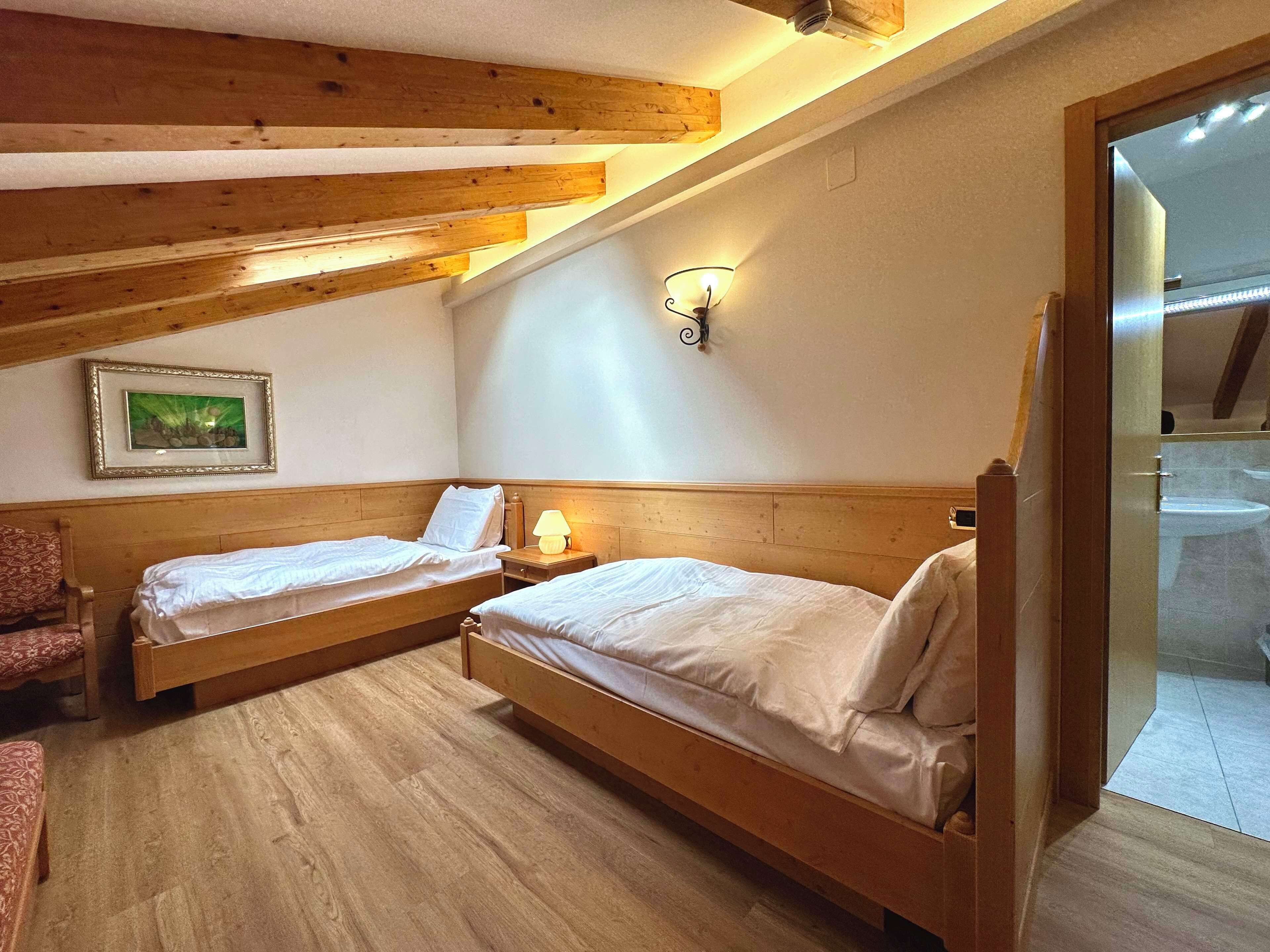 Une chambre à coucher avec deux lits en bois, une table de chevet avec une lampe, un tableau encadré au mur et une poutre en bois au plafond.