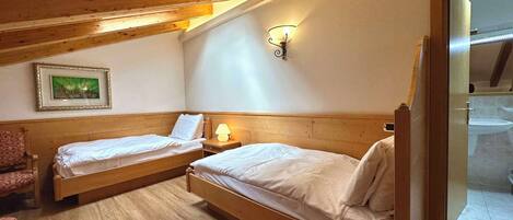 Une chambre à coucher avec deux lits en bois, une table de chevet avec une lampe, un tableau encadré au mur et une poutre en bois au plafond.