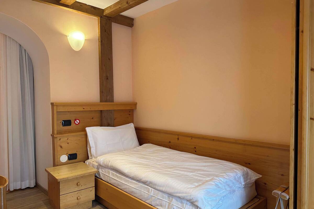 Un dormitorio con una cama de madera, una mesita de noche, una lámpara fijada a la pared y una viga de techo de madera.
