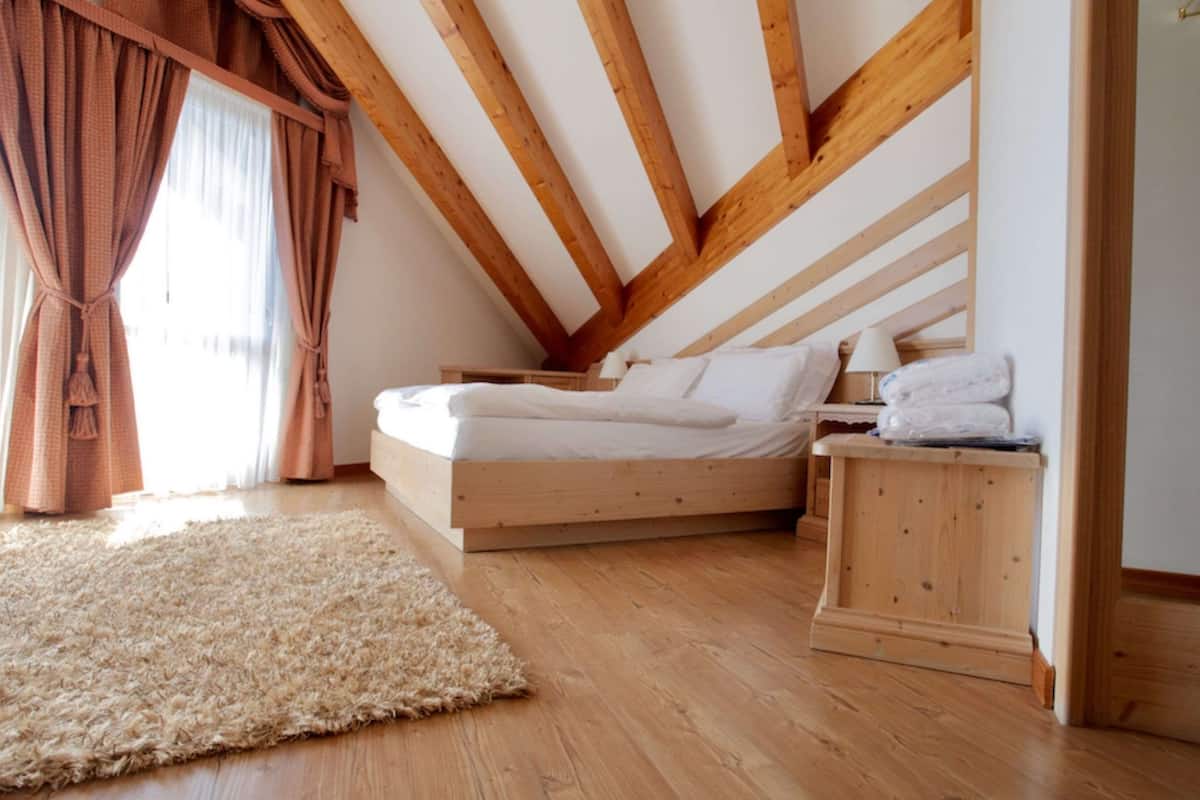 Un dormitorio con techo de madera, una cama, una mesita de noche con lámpara y una alfombra.