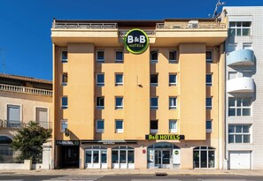 A B&B hotel with a central sign, multiple windows, and a parking entrance.