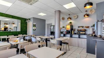 A modern cafe with tables and chairs, a counter with food display, and a green wall.