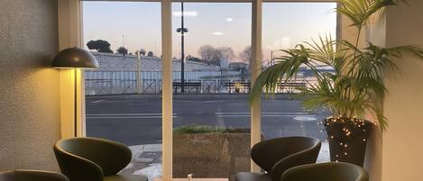 Un espacio de descanso con vista a una calle y un edificio. Hay dos sillas y una mesa con una botella y un menú.