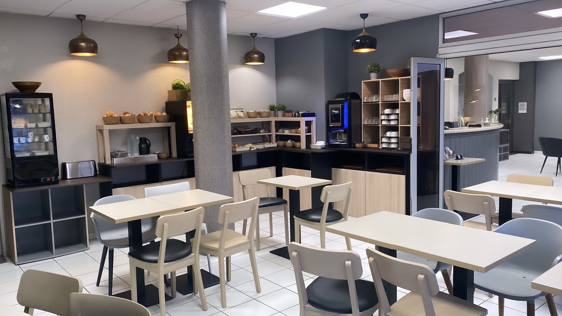 Un café moderne doté de plusieurs espaces de détente, d’une machine à café et d’étagères où sont disposés des bols et des tasses.