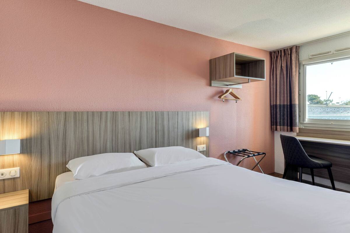 A hotel room with a bed, bedside table, lamp, and a window with curtains.