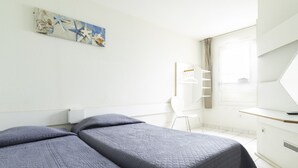 Ein Hotelzimmer mit zwei Betten, einem Schreibtisch, einem Stuhl und einem fensterbelaubten Fenster.