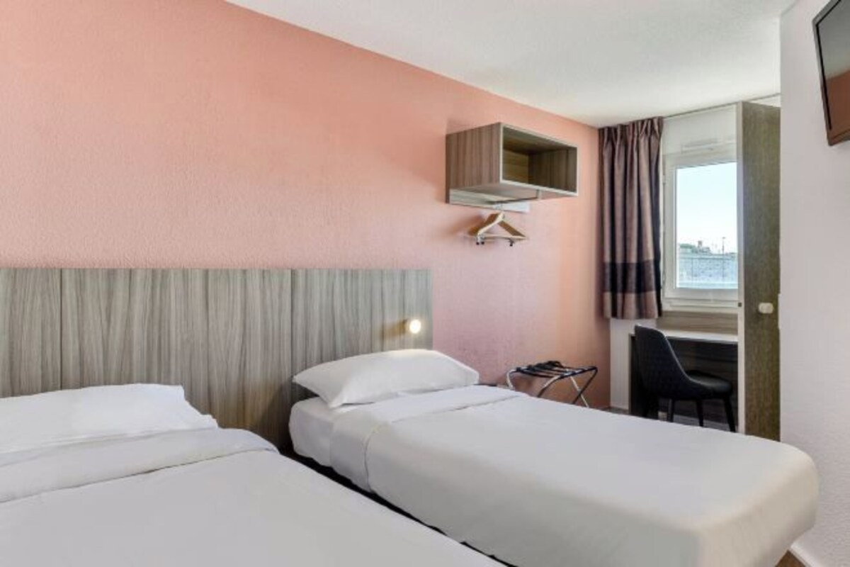 Habitación de hotel con dos camas, un escritorio y una ventana con cortinas.