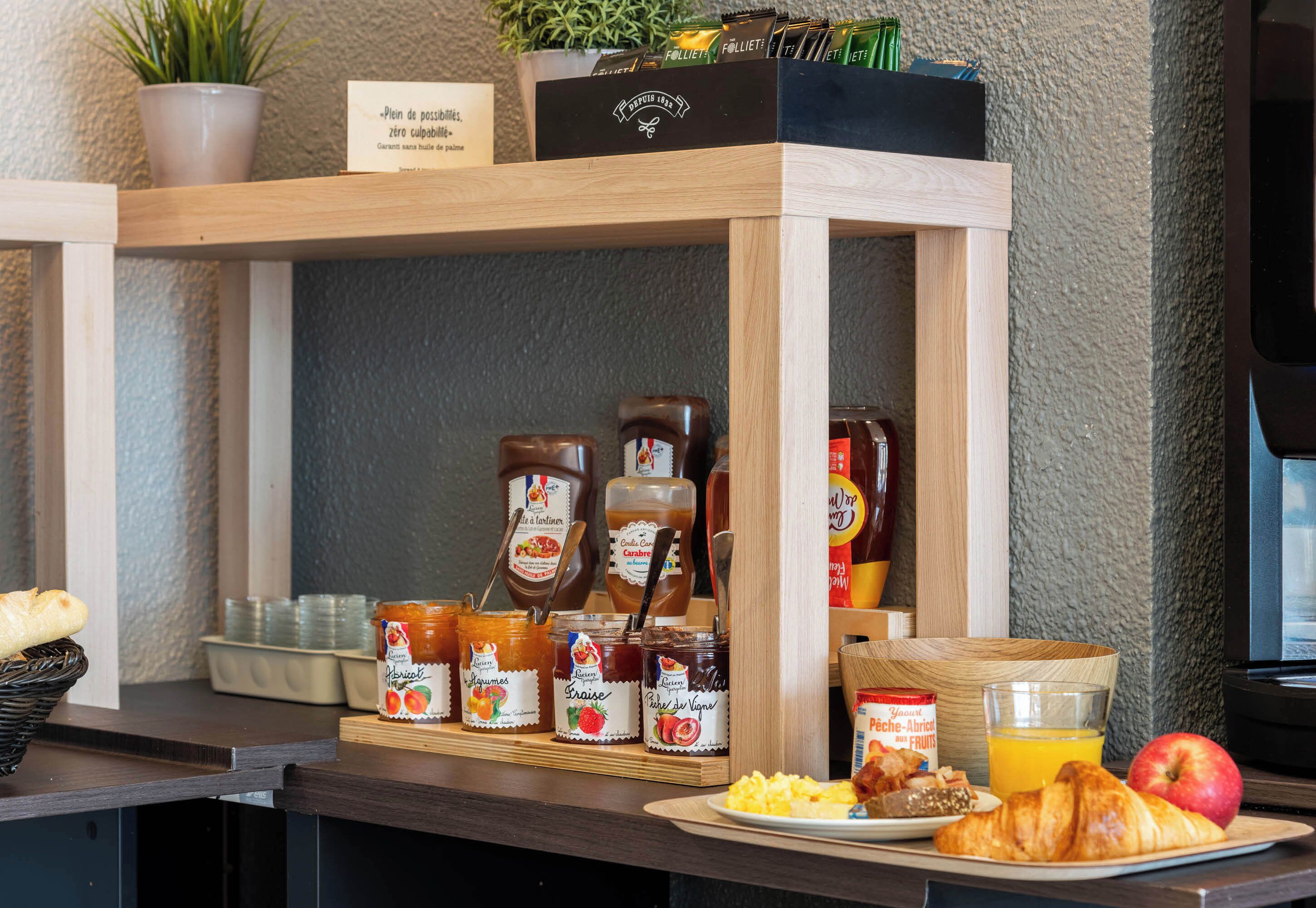 A breakfast buffet with various jams, honey, and a plate of croissants, orange juice, and an apple.