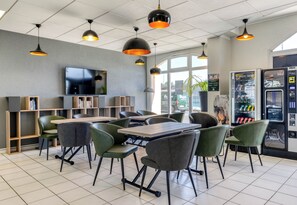 A modern cafe with a large TV, multiple tables, chairs, and a vending machine.
