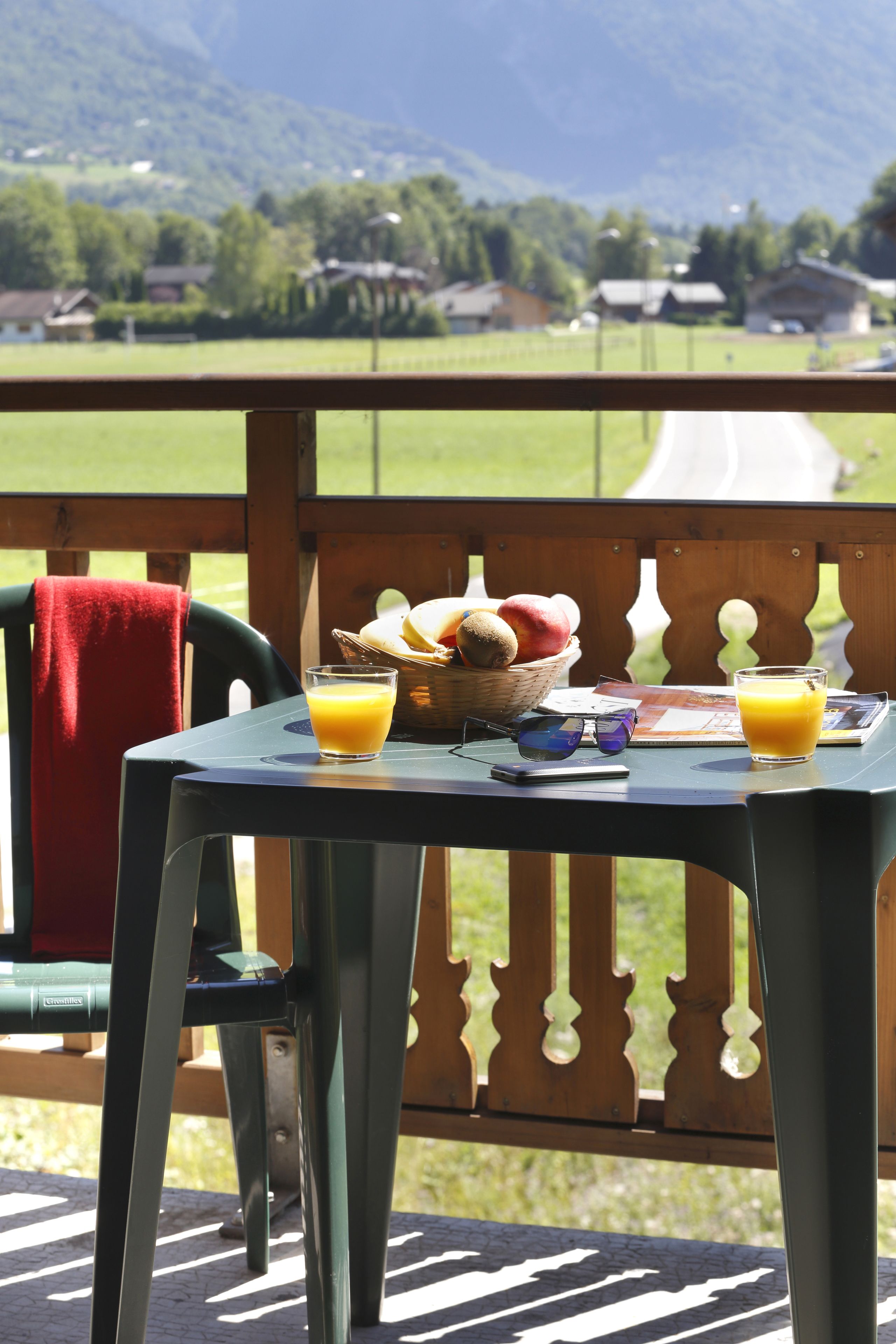 Une table avec des aliments pour le petit-déjeuner, une chaise et une vue sur un paysage verdoyant parsemé de maisons.