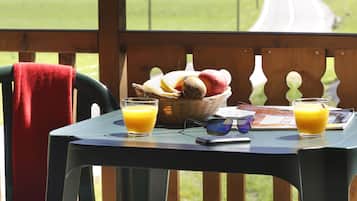 Une table avec des aliments pour le petit-déjeuner, une chaise et une vue sur un paysage verdoyant parsemé de maisons.