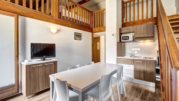 A compact kitchen with a dining area, wooden accents, and a built-in microwave. - Résidence Grand Massif - Vacancéole (Morillon)