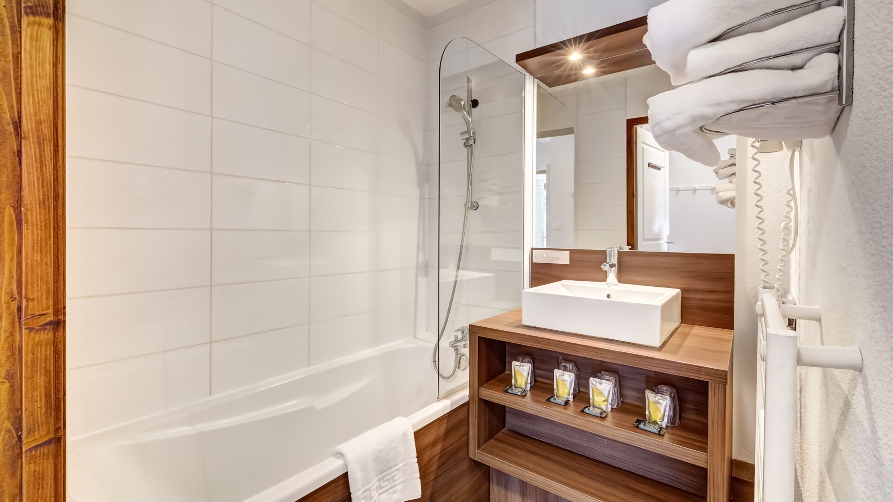 Un baño moderno con bañera, tocador de madera con lavabo y cabina de ducha con mampara de vidrio.