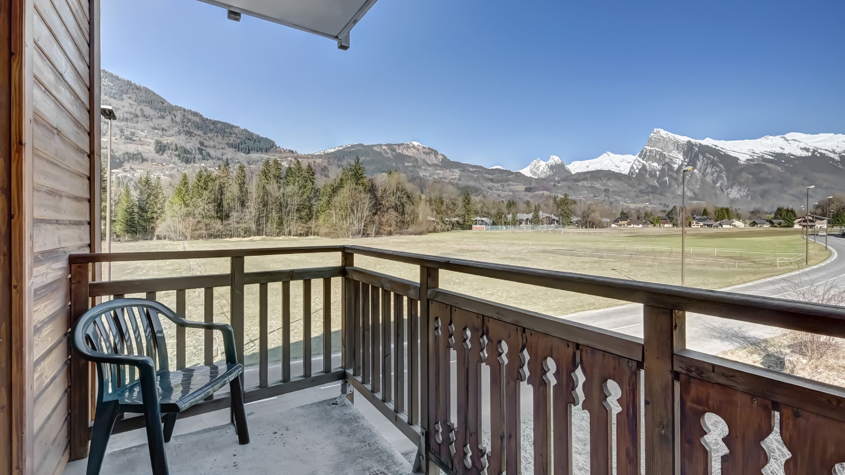 A balcony with a view of a mountainous landscape, a grassy field, and a road.
