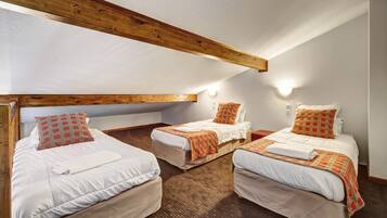 A room with three beds, wooden beams, and a sloped ceiling.
