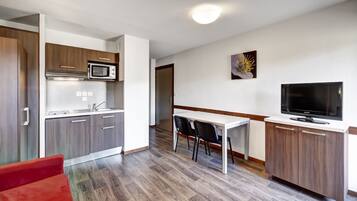 A compact kitchen with a microwave, sink, and cabinets, a dining area with chairs, and a TV on a cabinet.