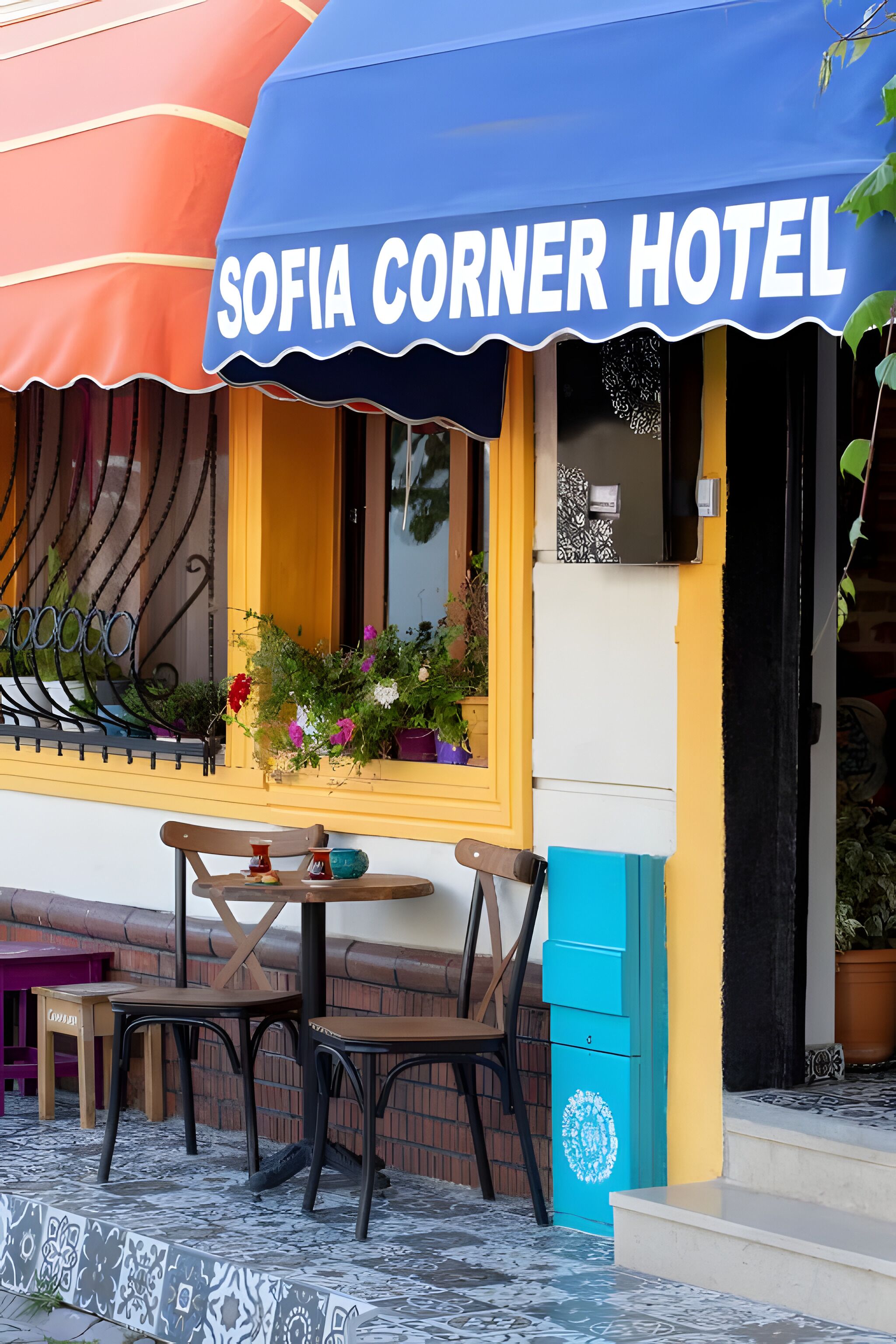 A corner hotel with a blue awning, outdoor seating, and a window display of flowers.