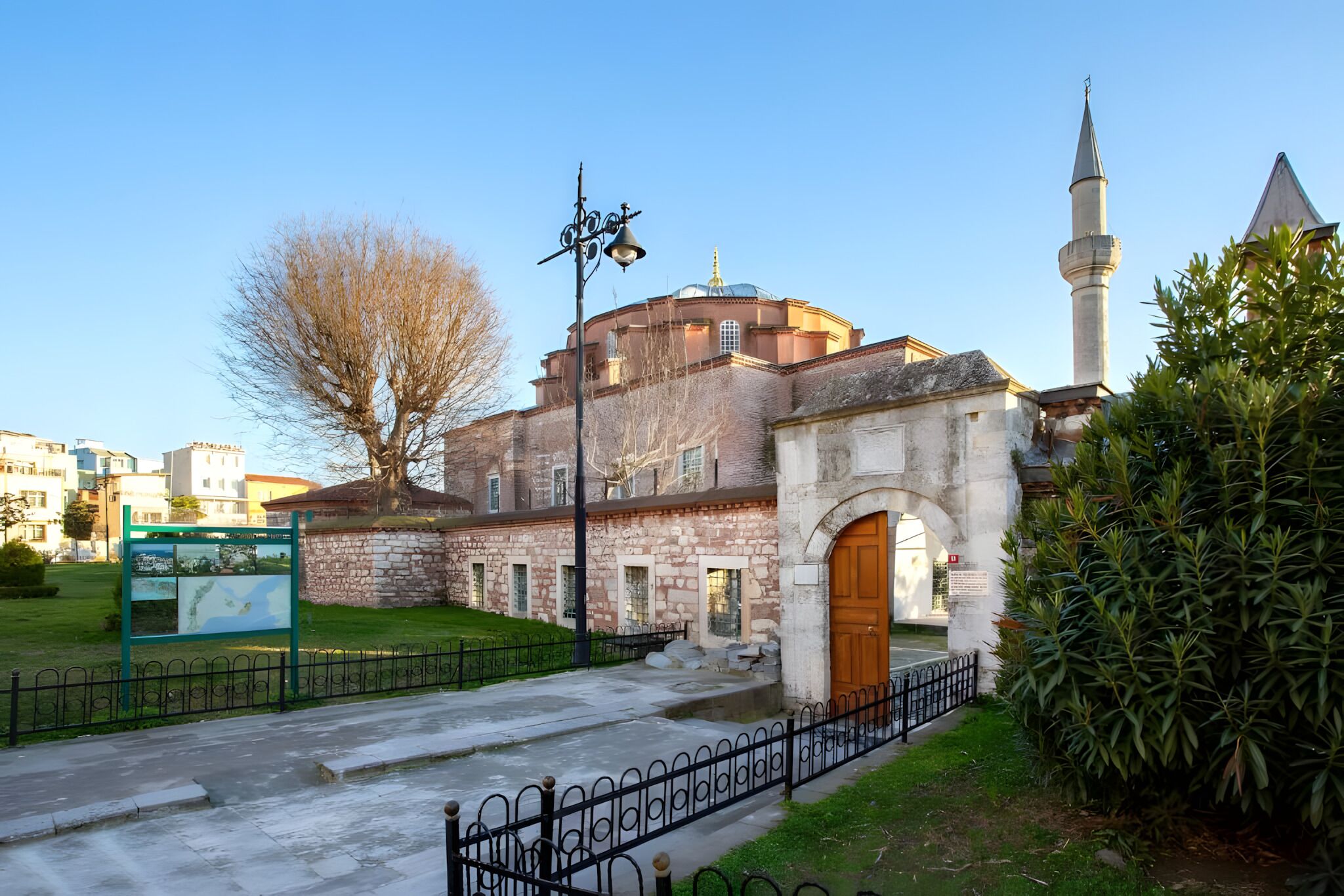A historic building with a prominent dome and a tall minaret, surrounded by a well-maintained garden and a paved walkway.