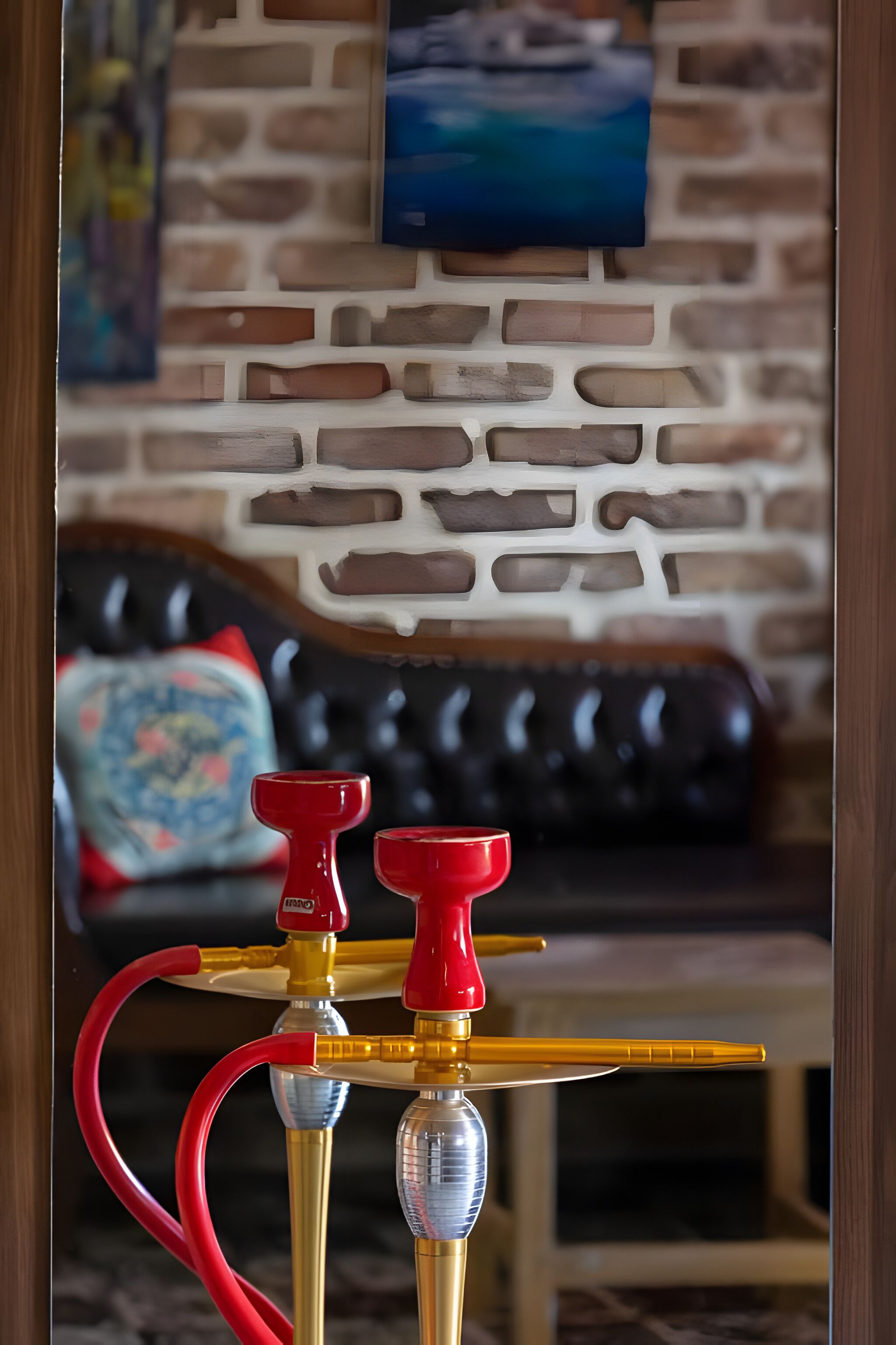 A hookah with red and gold accents, a brick-patterned wall, and a black leather sofa with a patterned cushion.