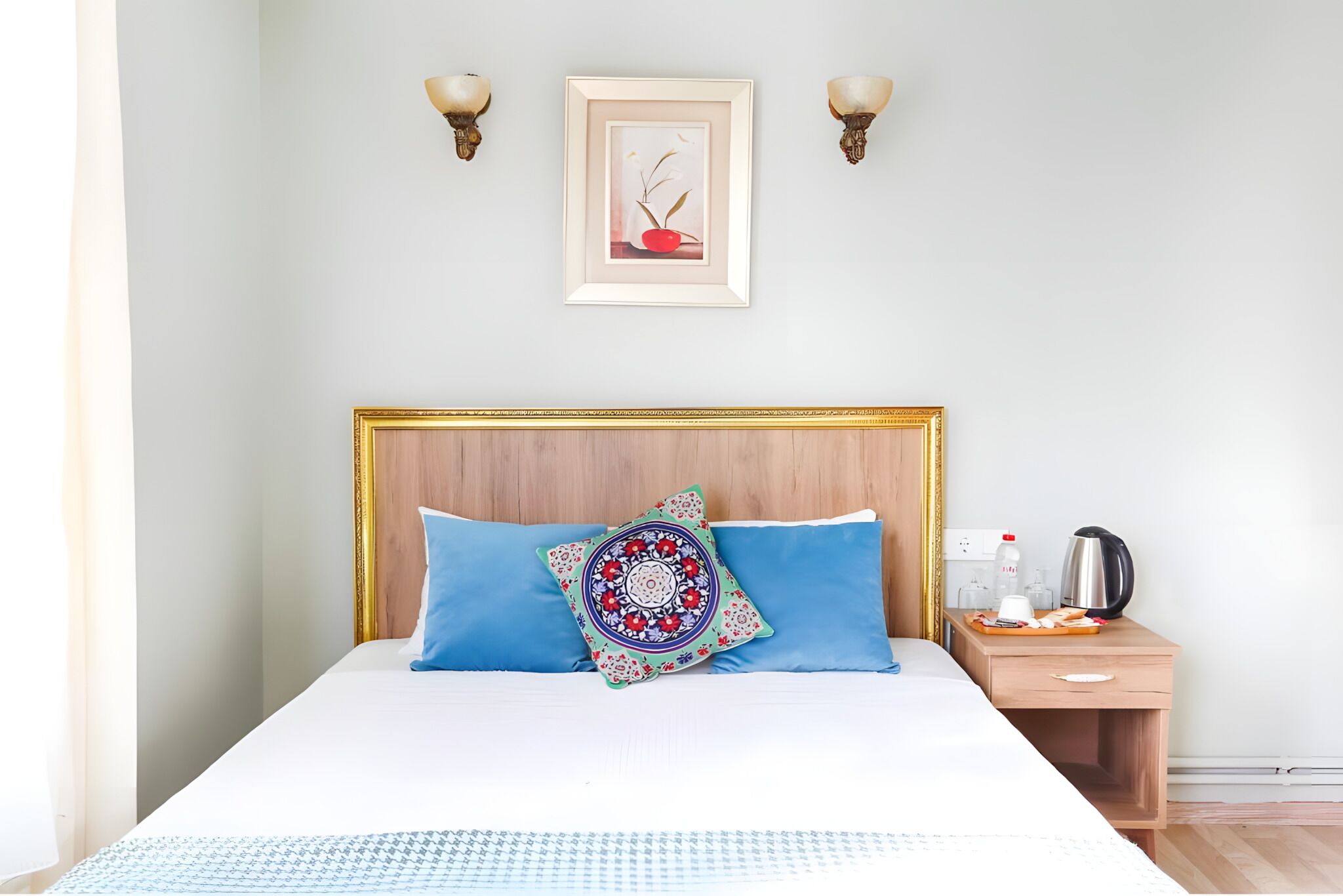 Una cama bien hecha con ropa de cama azul y blanca, un cojín decorativo y una obra de arte enmarcada en la pared.