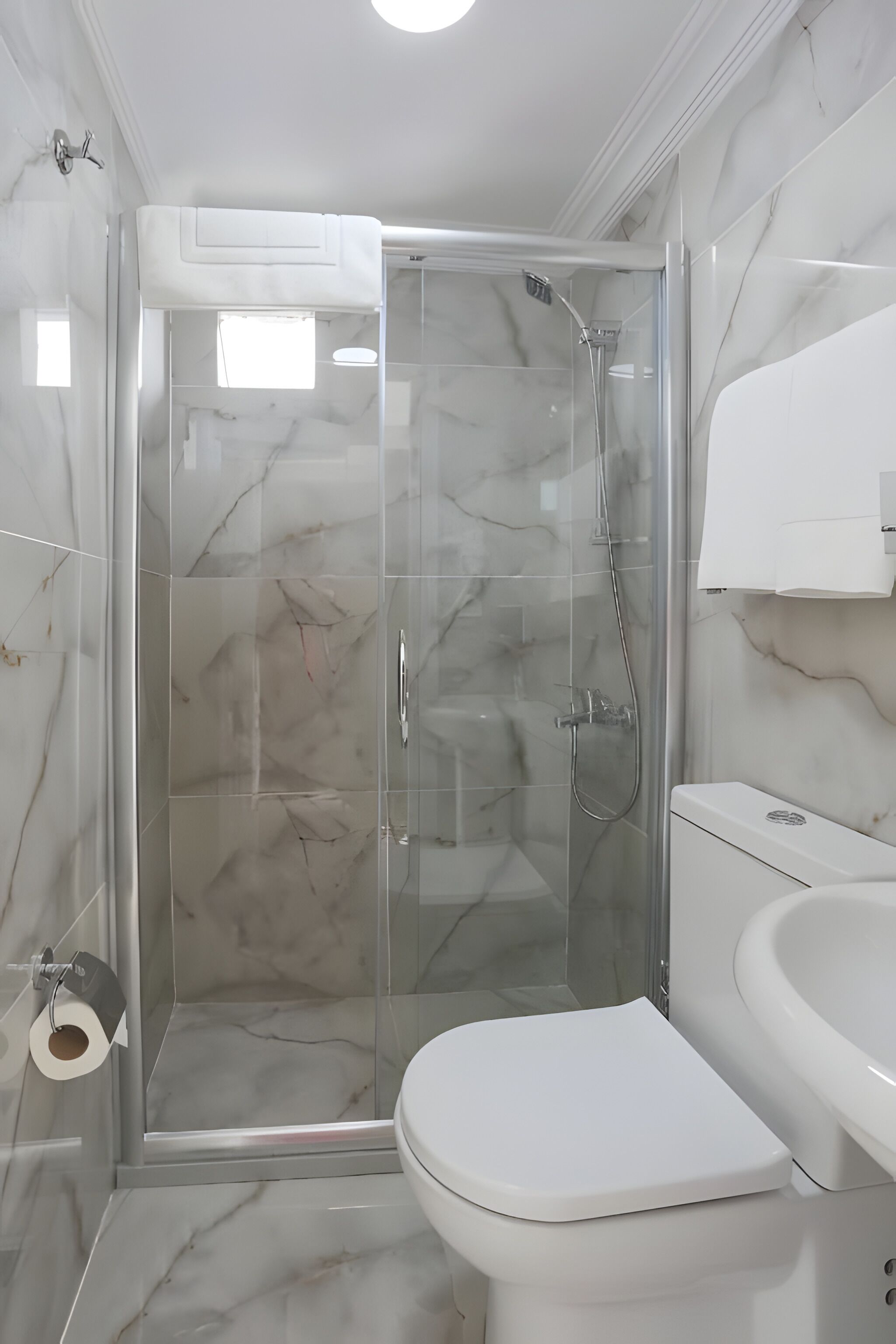 A bathroom with a glass-enclosed shower, a white toilet, and a marble-tiled floor.