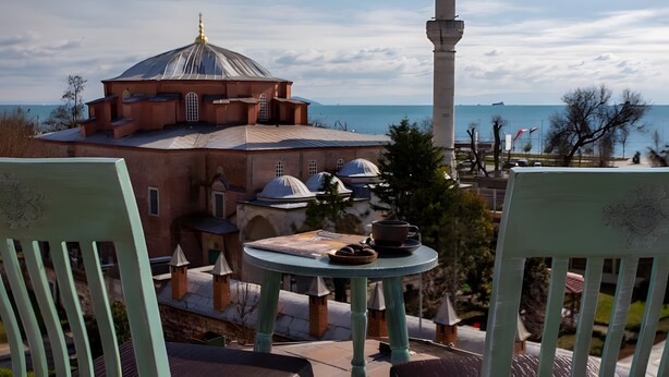 A view of a building with domed architecture, a tall minaret, and a table with a plate of cookies and a cup. - Sofia Corner Hotel (Istanbul)