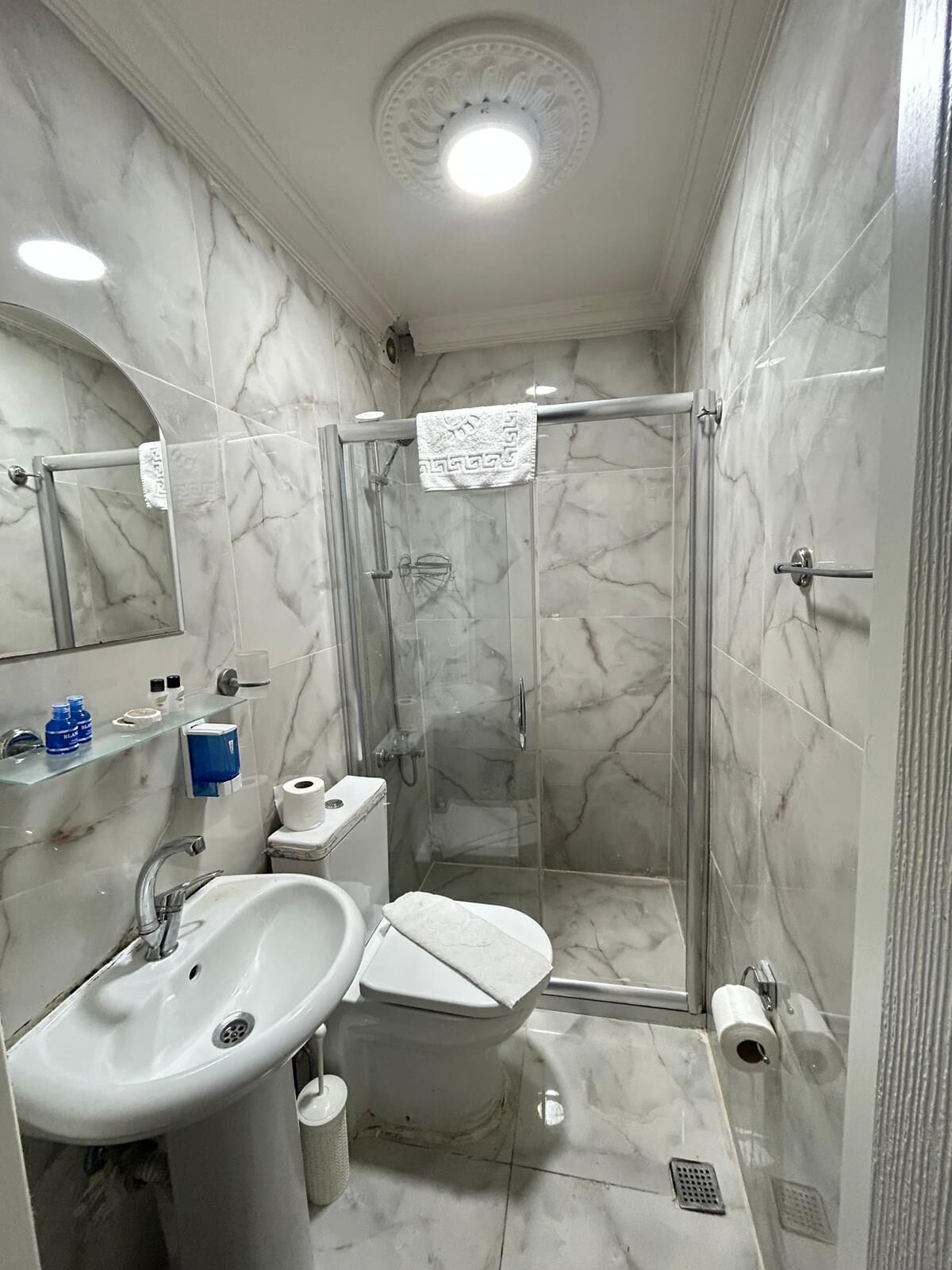 A bathroom with a marble floor, a glass shower enclosure, a sink, a toilet, and a mirror.