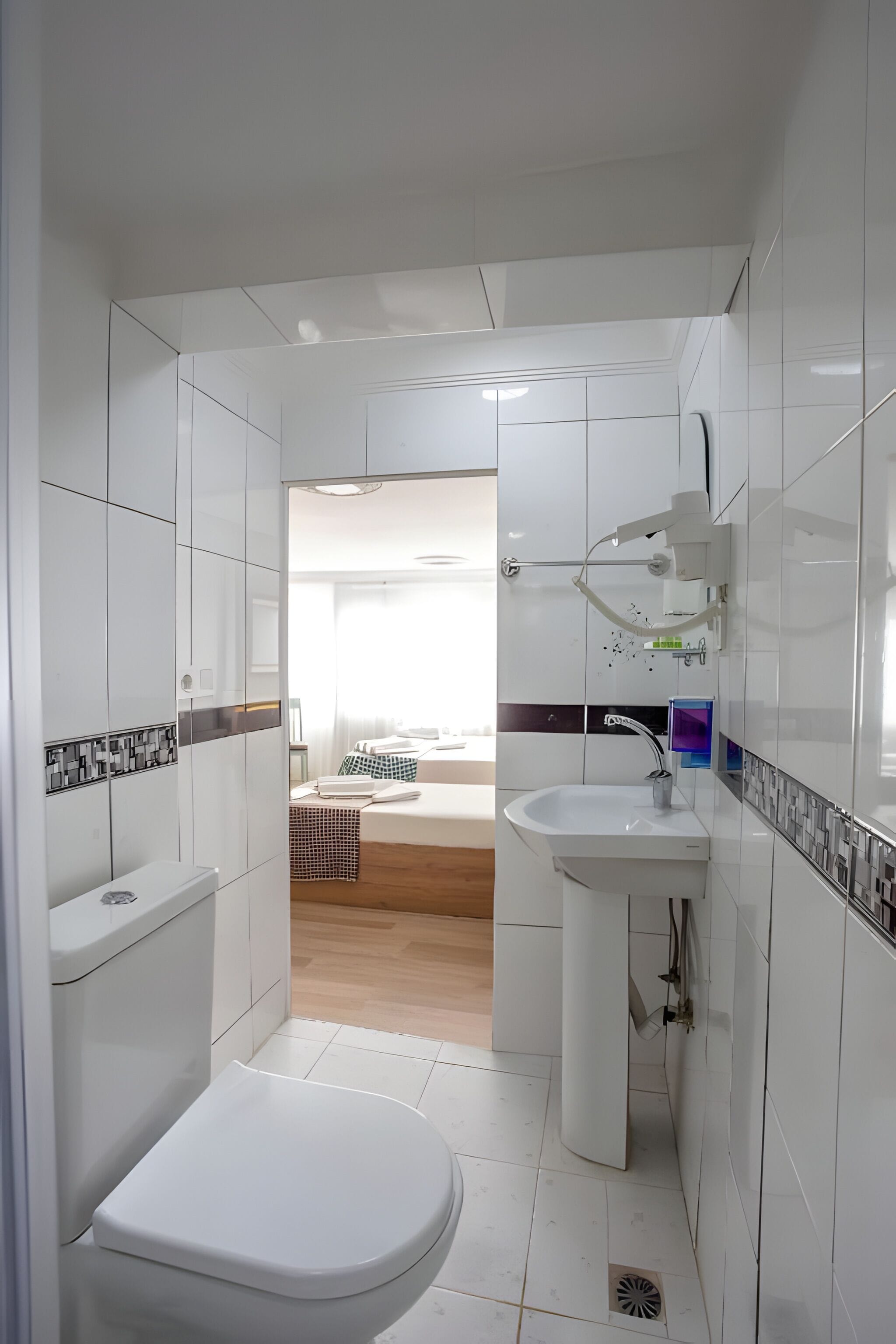 Une salle de bain moderne équipée de toilettes, d’un lavabo et d’une douche. Elle est carrelée de carreaux blancs et possède un plancher en bois.