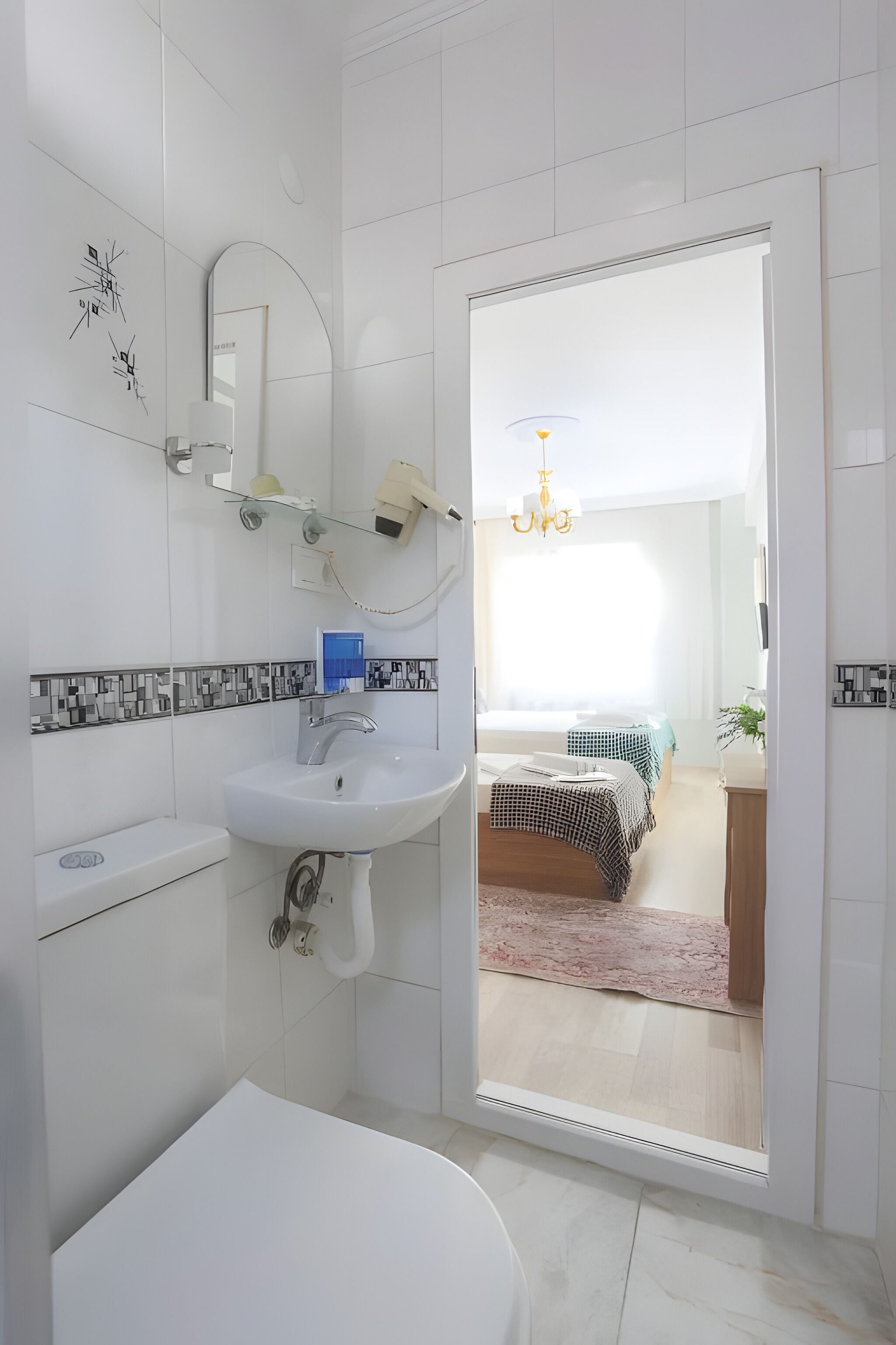 Ein modernes Badezimmer mit Waschbecken, Spiegel und Toilette. Eine Tür führt in ein Schlafzimmer mit Bett und einer Kronleuchter.