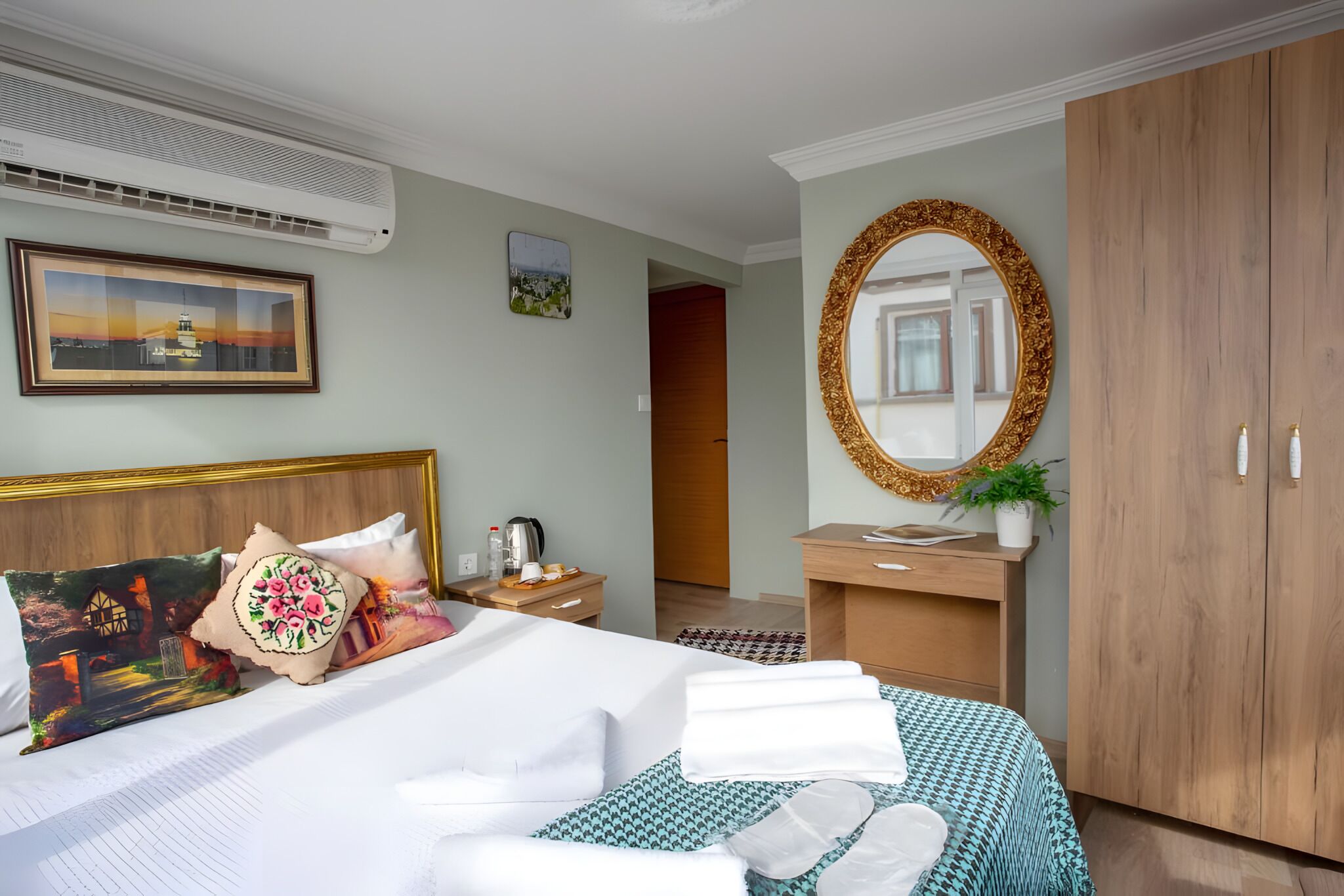 Quarto de hotel com uma cama, guarda-roupa de madeira, escrivaninha com espelho e um quadro na parede.
