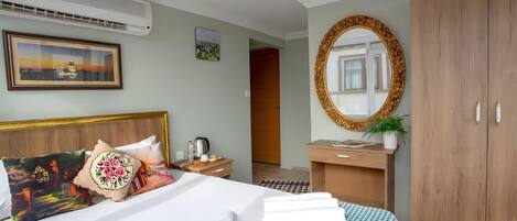 Quarto de hotel com uma cama, guarda-roupa de madeira, escrivaninha com espelho e um quadro na parede.