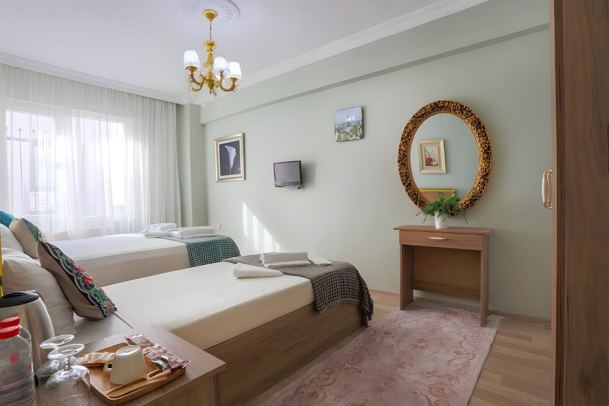 A hotel room with two beds, a desk, a mirror, and a chandelier.