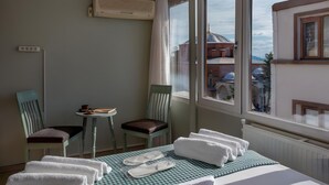 A hotel room with a bed, two chairs, a small table with a cup and a book, and a window with a view of buildings. - Sofia Corner Hotel (Istanbul)