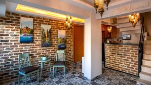 A hotel lobby with a brick wall, two paintings, a reception desk, and a staircase. - Sofia Corner Hotel (Istanbul)