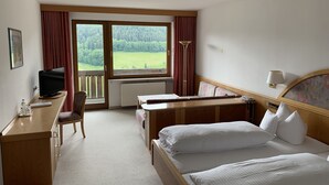 Habitación de hotel con cama, escritorio, silla y vista a un paisaje verde a través de amplias ventanas.