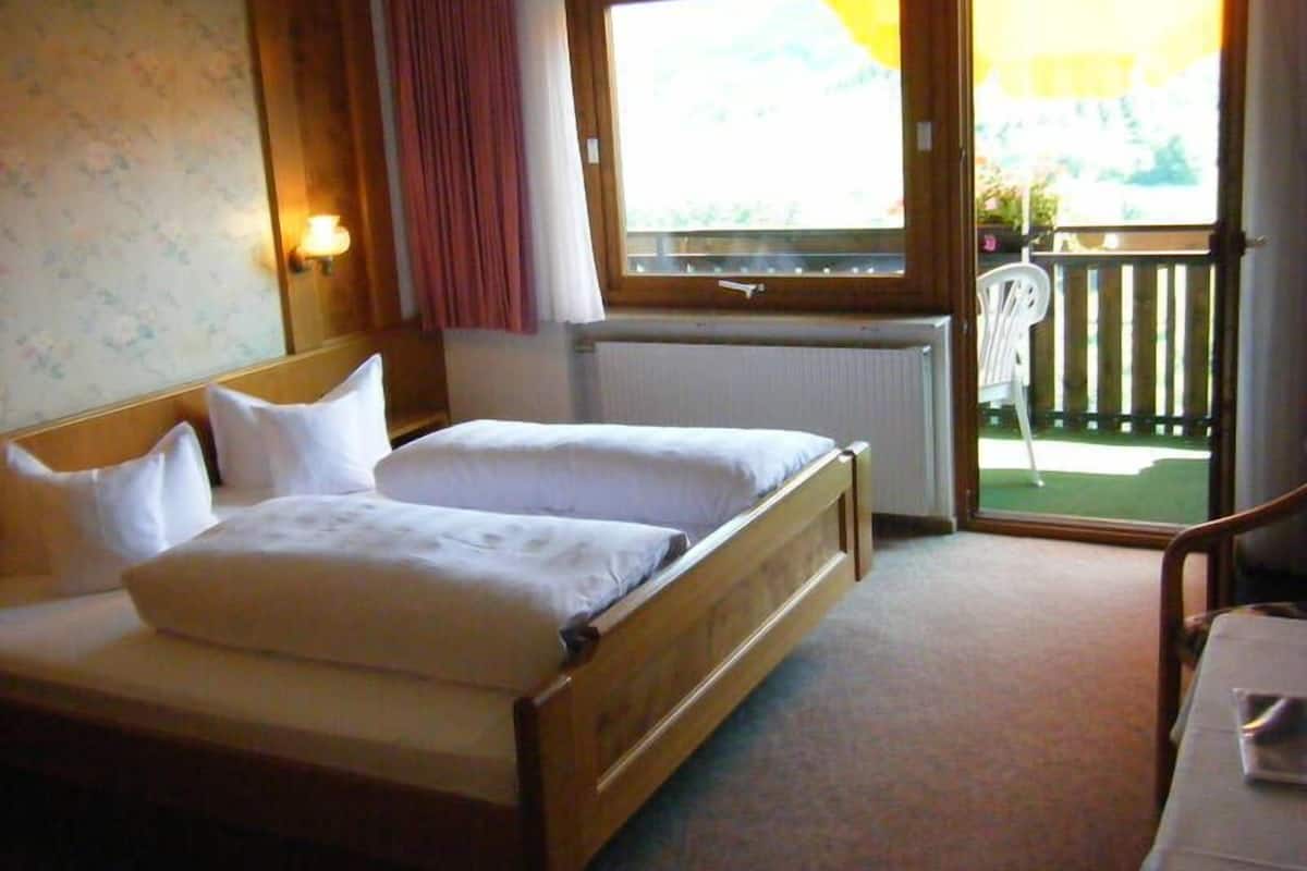 A double bed with wooden headboard, a window with a view of a balcony, and a radiator.