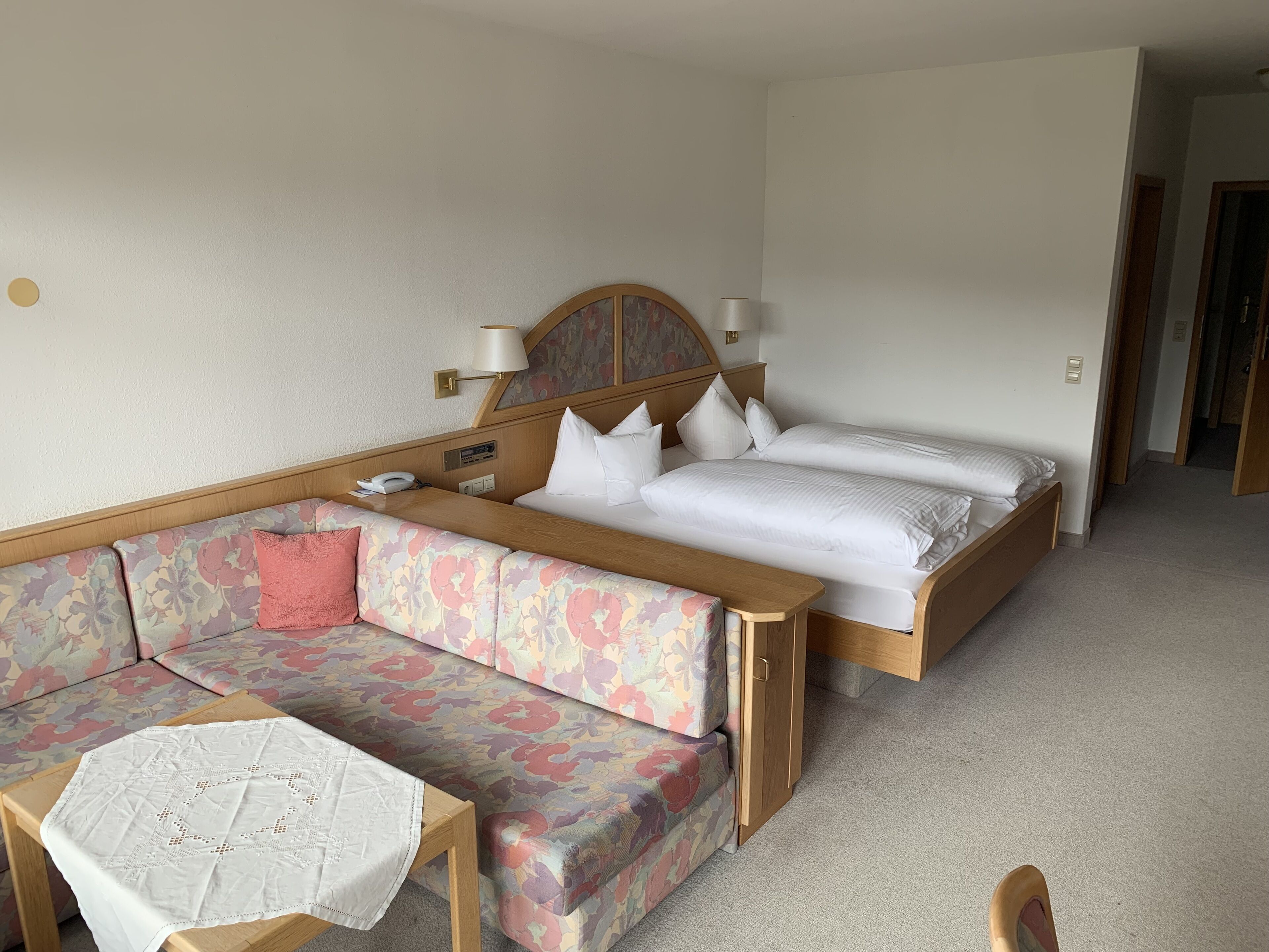 A hotel room with a wooden bed, a floral sofa, and a small table with a white tablecloth.