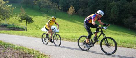 Two cyclists on a paved path with a grassy area and trees in the background.