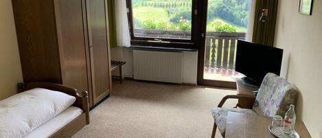Une chambre avec un lit, un bureau avec un ordinateur portable, une télévision et une vue sur un paysage verdoyant par la fenêtre.