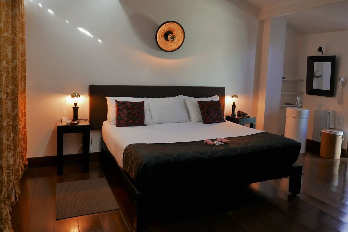 A neatly made bed with white and red pillows, a dark headboard, and two bedside tables with lamps.