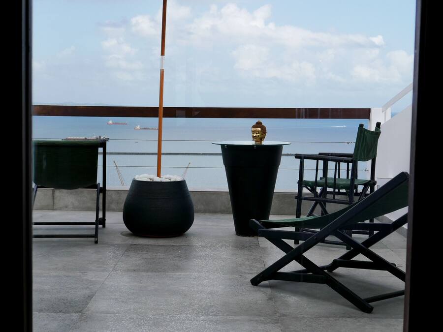 Ein Balkon mit Meerblick, eine Buddha-Statue, ein grüner Stuhl und ein schwarzer Topf.