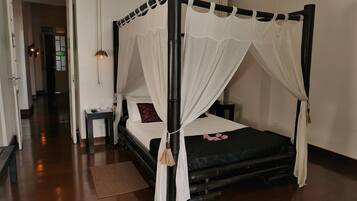 Un lit à baldaquin, une table de chevet avec une lampe et un banc dans une chambre d’hôtel.