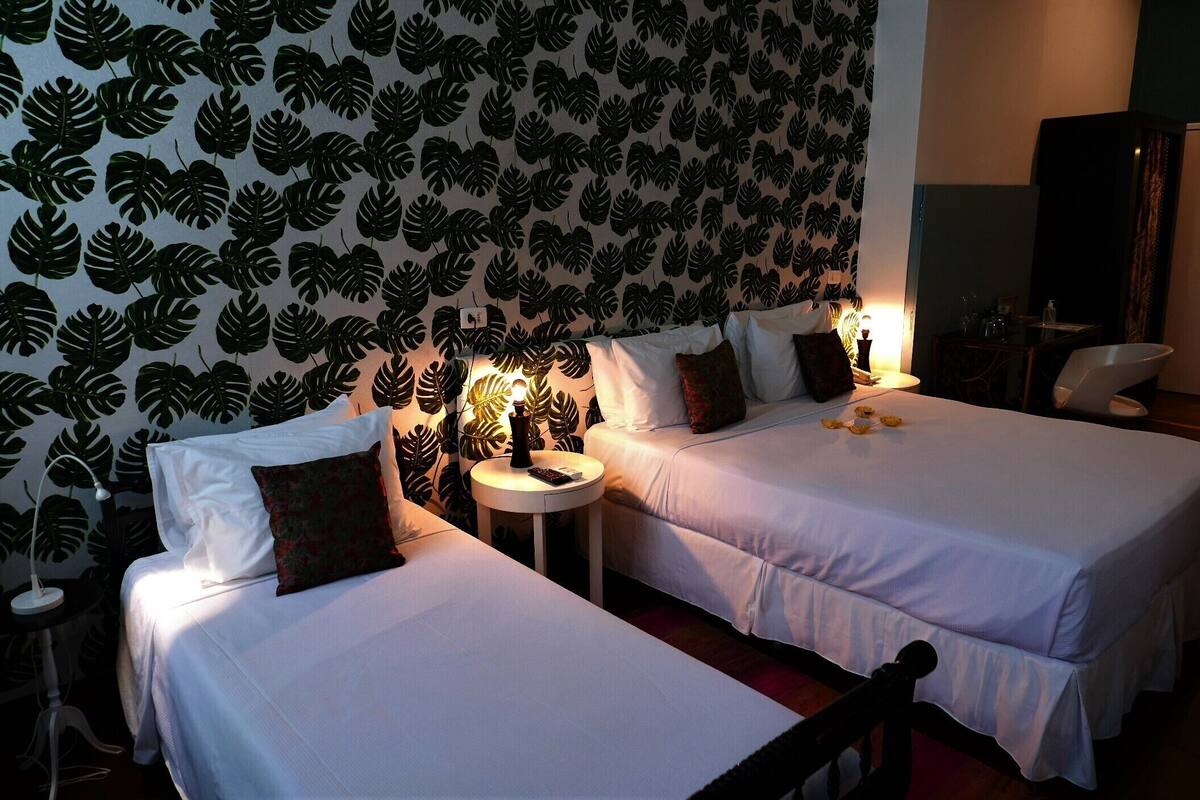 A hotel room with two beds, a small round table with a lamp, and a large mirror.