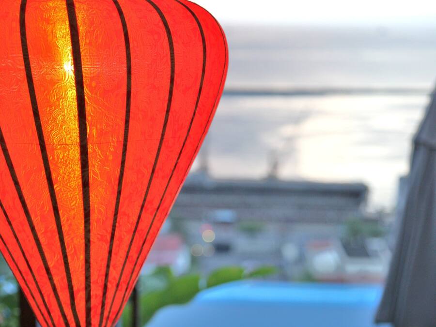 A red lantern hanging over a pool area with lounge chairs and a view of a bridge in the background.