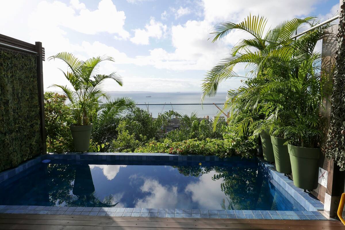 A pool with a view of the sea, surrounded by lush greenery and potted plants.
