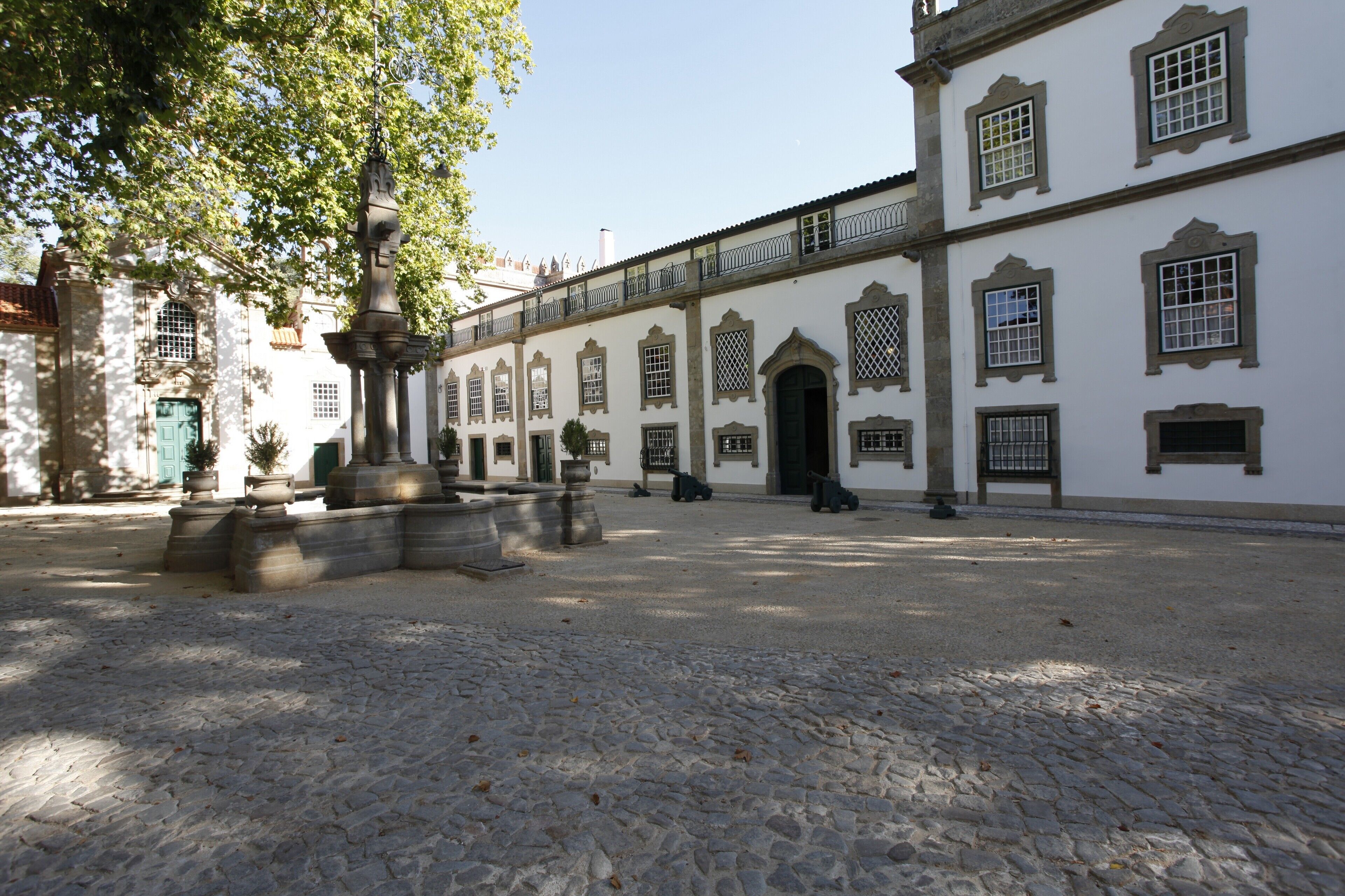 A courtyard with cobblestone flooring, a fountain, and a building with arched windows and a balcony.