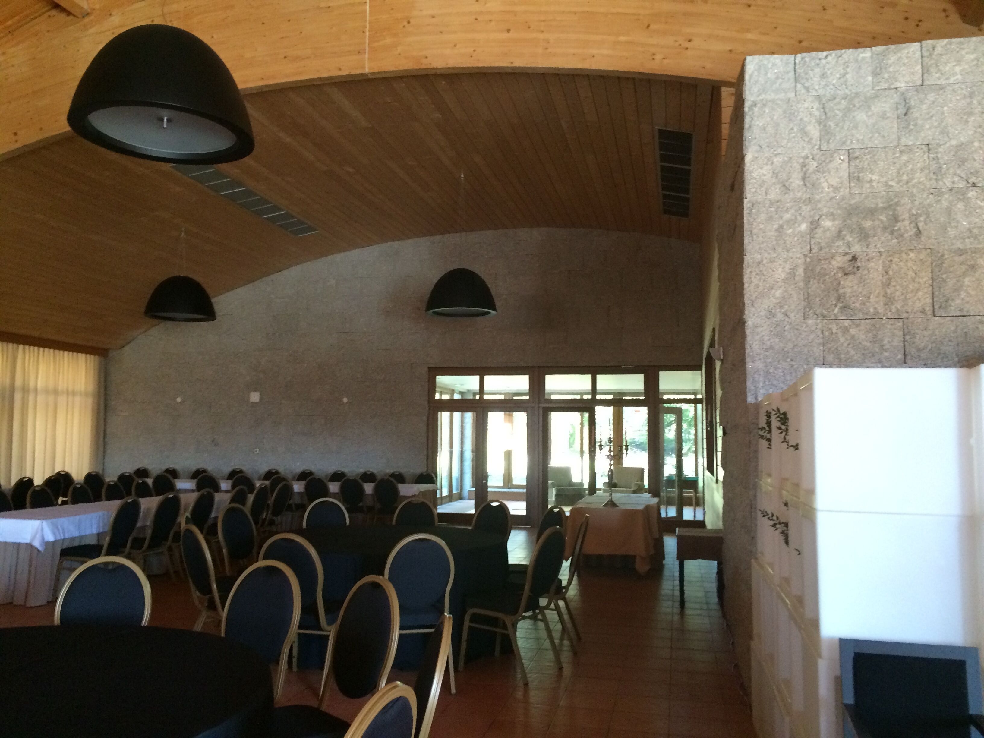 Un salón amplio con filas de sillas y mesas, techos altos de madera y ventanas grandes.
