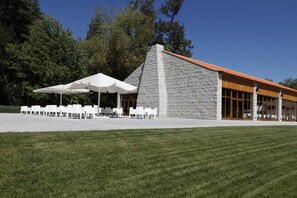 A building with a stone facade and a red roof, surrounded by a grassy area with white chairs and umbrellas. - Parador Casa da Ínsua (Penalva Do Castelo)