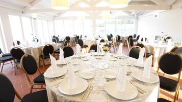 A banquet hall with round tables set for a formal event, featuring white tablecloths, gold cutlery, and black chairs.